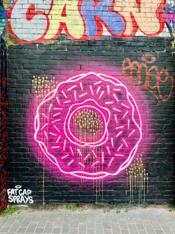 Neon-Graffiti eines Donuts auf schwarzer Backsteinwand – leuchtend pink mit goldenen Drips
